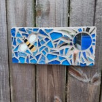B + A mosaic of a bee and the sun. The bee is on the left and the sun is on the right. The sun is made of mirrored glass. The background is various shades of blue.