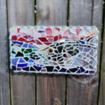 Pride A mosaic of a snook. The mosaic is made of colored glass and mirrored glass, with a glass bead border. It is wall art that is fastened to a wood fence.