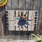 Solar Shards Mosaic wall hanging of a mirrored sun.Vertical lines of tile and stones in tan to brown colors make up the background with the sun in the middle. The piece measures 18" x 12.5" x 1.25".